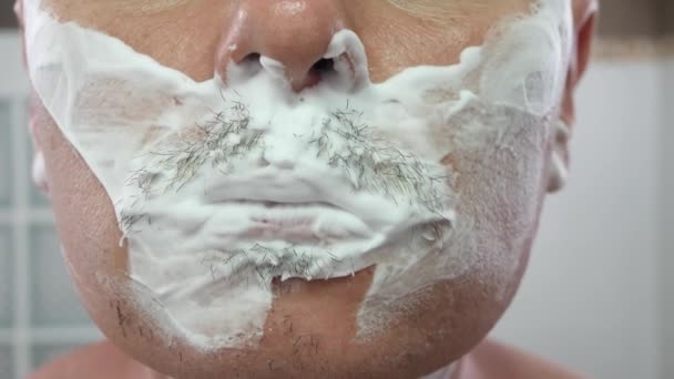 Beau jeune homme avec de la mousse sur le visage se raser à l'aide d'un rasoir - Séquence, vidéo