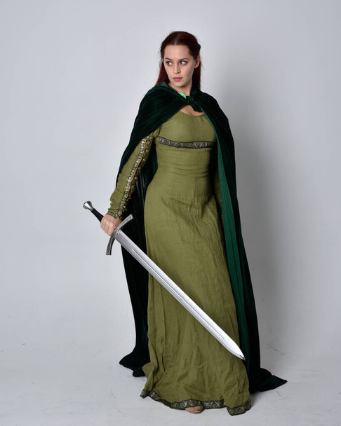 retrato de comprimento total da menina de cabelos vermelhos vestindo celta, vestido medieval verde com capa de veludo fantasia. pose de pé isolado contra um fundo de estúdio. - Foto, Imagem