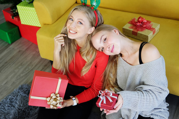 Χαμογελώντας στην εφηβεία. Καυκάσια κορίτσια κάθονται στο πάτωμα και κρατούν μεγάλα κουτιά δώρων στο Χριστουγεννιάτικο πάρτι. Τρόπος ζωής των λεσβιών στις διακοπές έννοια. - Φωτογραφία, εικόνα