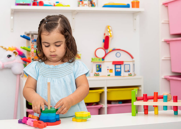 Дворічна дівчинка з кавказького походження, грає і вчиться дуже зосереджено на деяких освітніх дерев'яних іграшках у дитячому садку.. - Фото, зображення