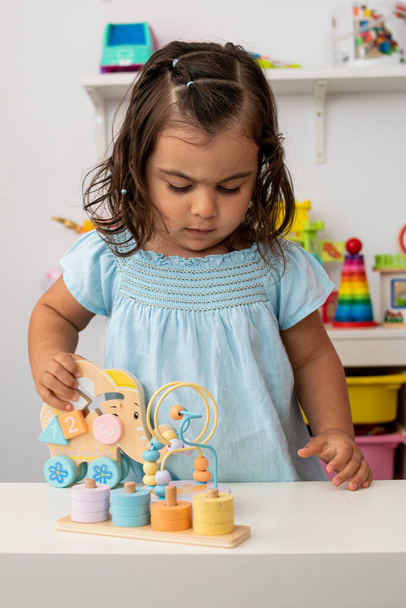 Twee-jarige meisje van blanke afkomst, zeer geconcentreerd, spelen met educatieve houten montessori speelgoed, waarmee ze leert tijdens het plezier in de kleuterschool. - Foto, afbeelding