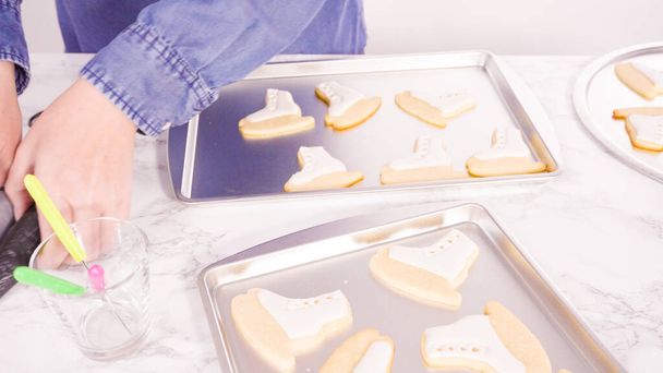 Decorating ice skate shaped sugar cookies with white color royal icing. - Photo, Image