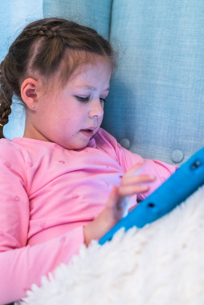 Маленька дівчинка читає книги на планшеті вдома
. - Фото, зображення