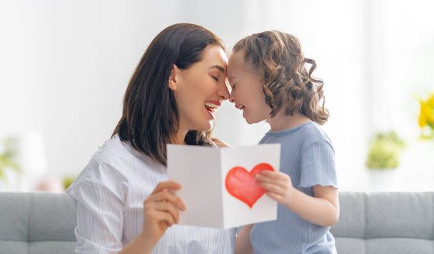 Happy mother's day! Child daughter is congratulating mom and giving her postcard. Mum and girl smiling and hugging. Family holiday and togetherness. - Foto, Imagen