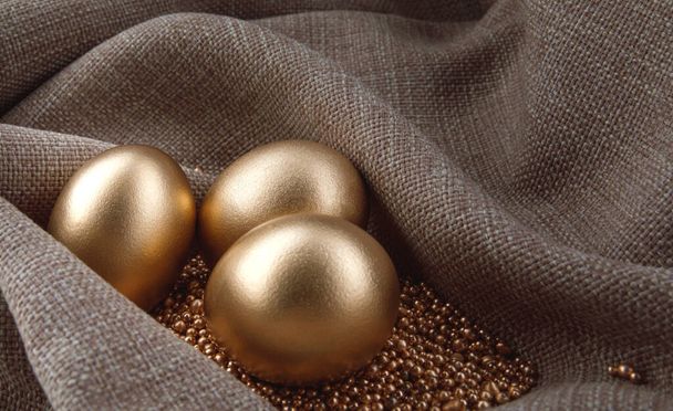 Τρία χρυσά αυγά σε χρυσή άμμο σε κύματα ιστού. - Φωτογραφία, εικόνα