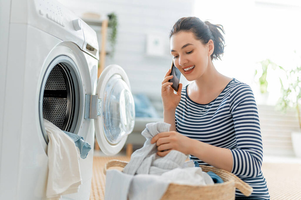 Beautiful young woman is smiling while doing laundry at home. - Foto, Imagen