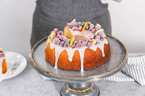 Snijd citroen cranberry bundt cake versierd met suiker cranberries en citroen wiggen op een taart standaard. - Foto, afbeelding