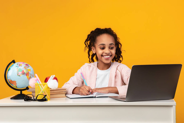 Portret uśmiechniętej czarnej dziewczyny siedzącej przy stole i piszącej - Zdjęcie, obraz