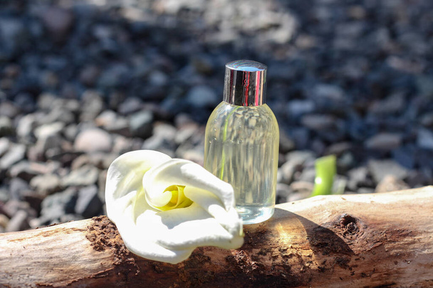 Bottiglia cosmetica trasparente in piedi su ramo d'albero circondato da fiore di calla giglio - Foto, immagini