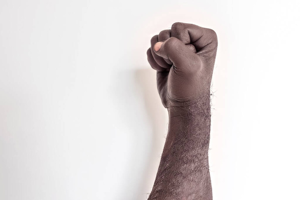 Αρσενικό χέρι σφιγμένο σε μια γροθιά σε λευκό φόντο. Ένα σύμβολο του αγώνα για τα δικαιώματα των μαύρων στην Αμερική. Διαδήλωση κατά του ρατσισμού - Φωτογραφία, εικόνα