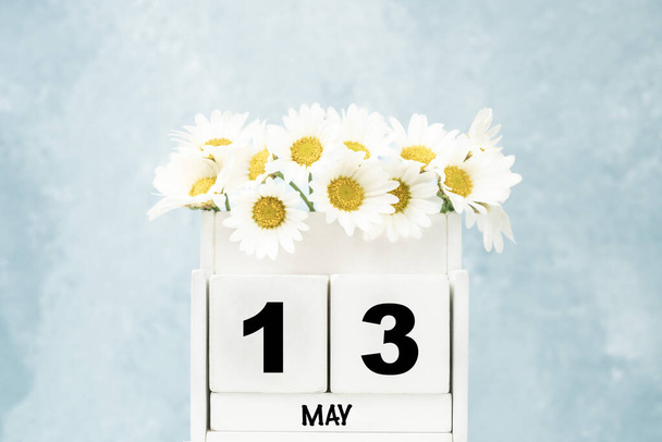 Witte kubus kalender voor mei met madeliefje bloemen over blauwe achtergrond met kopieerruimte - Foto, afbeelding