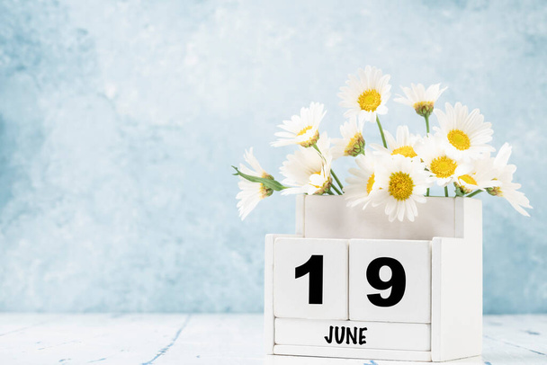 Calendrier cube blanc pour juin décoré de fleurs de marguerite sur fond bleu avec espace de copie - Photo, image