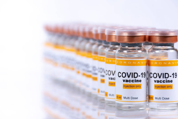 Dos filas de viales con vacuna contra el coronavirus sobre una mesa blanca con reflejos. Concepto de laboratorio o instalación sanitaria - Foto, Imagen