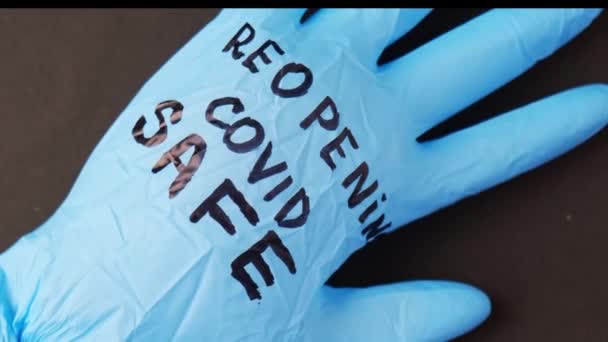 Opgeblazen blauwe latex chirurgische handschoen op zwarte achtergrond. Covid veilig heropenen. Open opnieuw tekst geschreven op medische handschoen. Nieuw normaal - Video