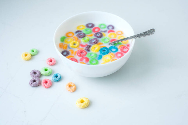 Cereali rotondi colorati riempiti di latte in un piatto bianco. Palle sparse su un tavolo bianco. Preparo la colazione. Foto di alta qualità - Foto, immagini