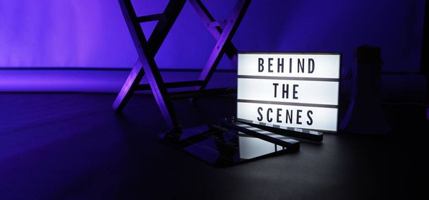 Behind the scenes light box. Text on cinema light box. Megaphone and director chair and movie slate beside. Background LED color. Camera in video production studio. Behind the scene concept. - Photo, Image