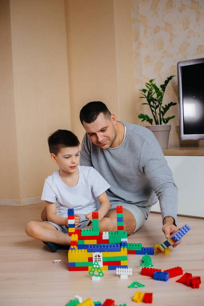A little boy together with his father is played by a constructor and builds a house. Construction of a family home. - Фото, изображение