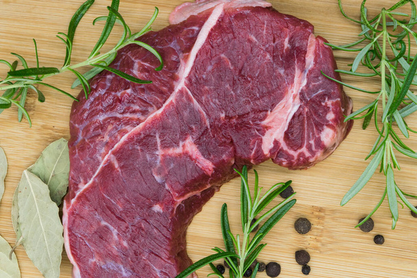 Steak de boeuf, vue de boeuf frais sur une planche de bois au romarin, poivre noir, feuille de toilette. - Photo, image