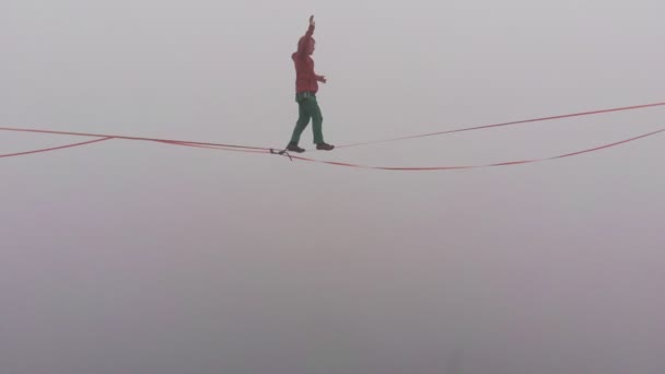 Close-up van een jonge man die op een strakke strop door de mist loopt. Slackline met verzekering. - Video