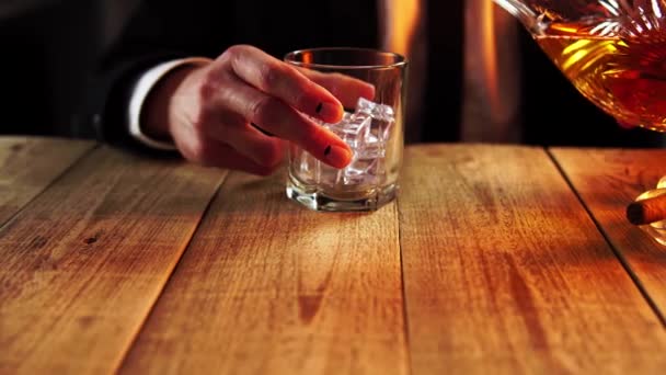 Een man die rust in een bar schenkt gouden alcohol uit karaf in een glas vol ijs in close-up - Video