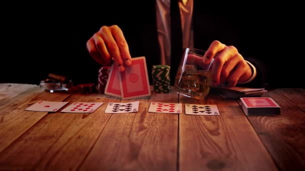 Man playing poker is waiting for his turn with glass full of whisky and two cards in his hands - Materiał filmowy, wideo