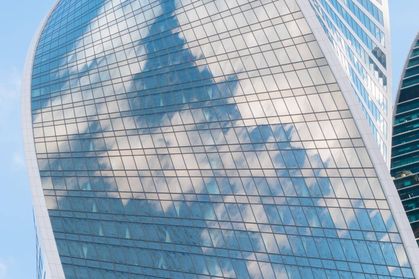 Αντανάκλαση των λευκών νεφών και του μπλε ουρανού σε γυάλινο τοίχο του σύγχρονου ουρανοξύστη - Φωτογραφία, εικόνα
