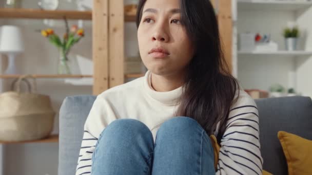 Zamyšlená asijská dáma sedí objímající kolena na pohovce v obývacím pokoji v domě pohled ven s pocitem osamělosti, Smutný depresivní teenager tráví čas sám doma, Společenská vzdálenost, Koronavirus karanténa. - Záběry, video
