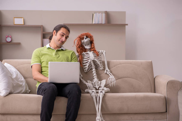 Junger Mann sitzt mit weiblichem Skelett auf dem Sofa - Foto, Bild