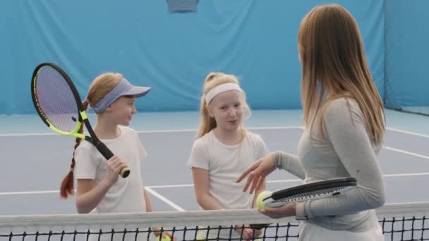 Közepes felvétel két csinos fehér lányról teniszütőkkel, akik a pályán edzenek női edzővel, és elmagyarázzák nekik a tenisz szabályait. - Felvétel, videó
