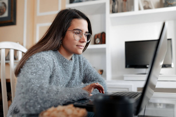Junge, fröhliche Frau im Pullover sitzt in ihrem Wohnzimmer und surft im Internet im Laptop. - Foto, Bild