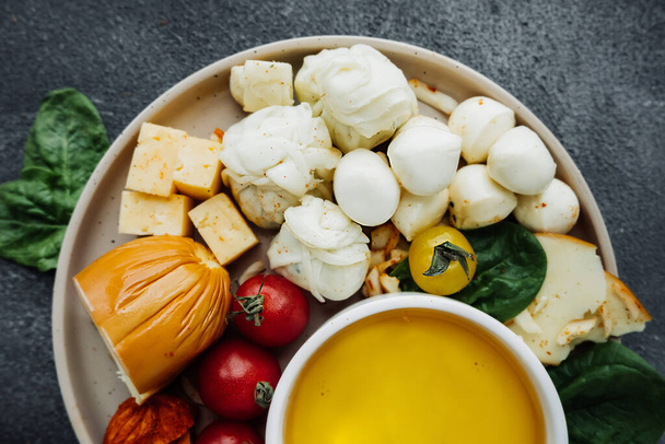 delicious cheese plate with different types of cheeses: mozzarella, Georgian, cottage cheese, smoked, parmesan, spicy, hard varieties. fresh tomatoes, cup of honey. serving snacks, selective focus - Photo, Image