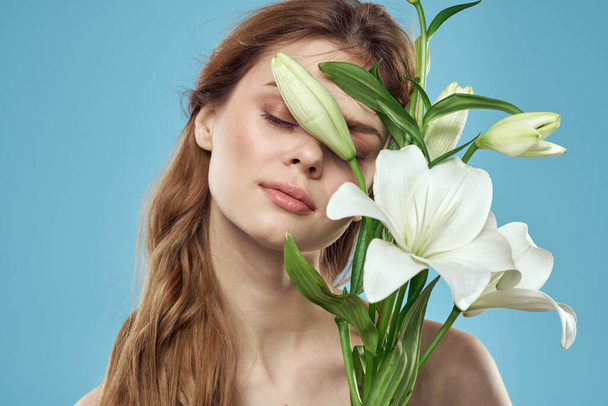Vrouw met een boeket witte bloemen op een blauwe achtergrond naakte schouders mooi gezicht - Foto, afbeelding