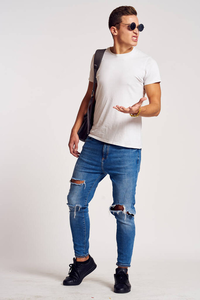 um homem com uma mochila nas costas em jeans t-shirt de comprimento total tênis e óculos em seu rosto - Foto, Imagem
