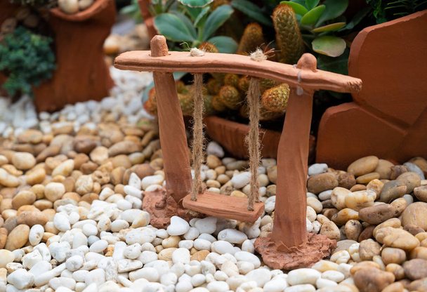 Μικρό handcraft από terracotta swing για διακόσμηση κήπου σε δίσκο κάκτο. - Φωτογραφία, εικόνα