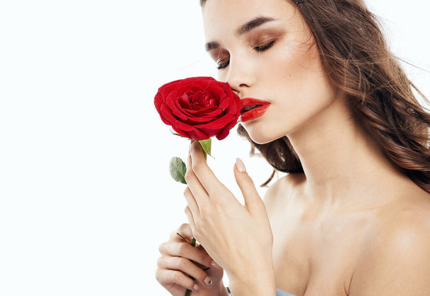 Charming brunette woman with bare shoulders and a fragrant flower near her face - Фото, изображение