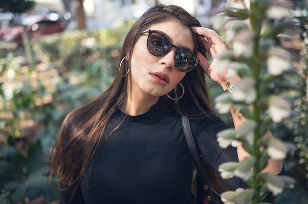 A cool sexy Mexican woman in sunglasses posing in a garden - Foto, afbeelding
