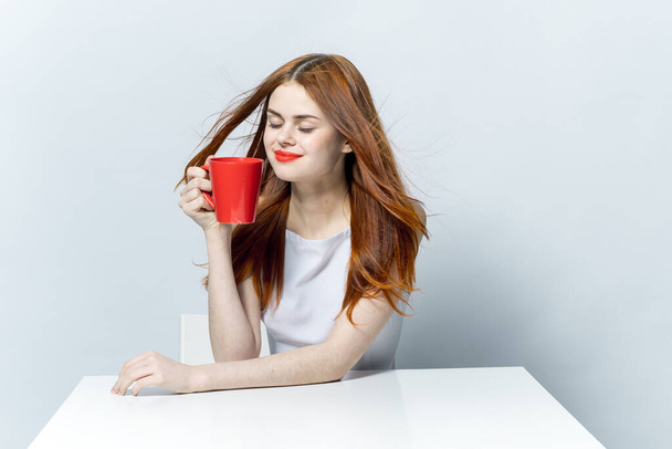 красива жінка тримає червоний кухоль в руці, сидячи за столом кави
 - Фото, зображення