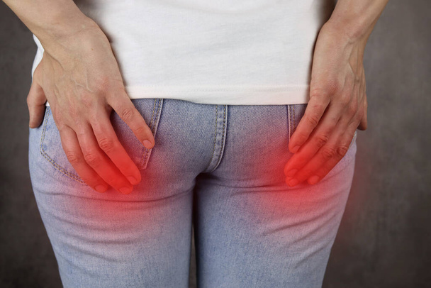 woman hand holding her painful butt, red pain area - Photo, Image