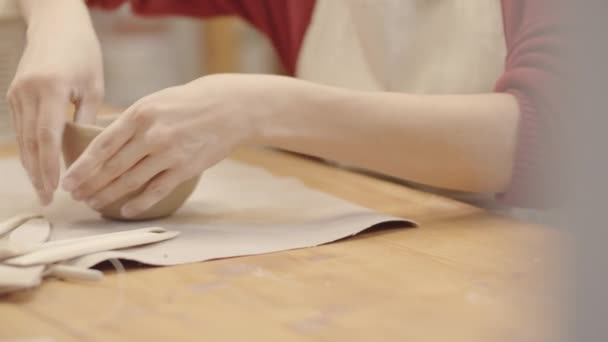 Nahaufnahme von kippenden Händen und Gesicht einer jungen kaukasischen Töpferin, die in einer Bastelwerkstatt Tonschalen modelliert, sie mit einer Hand hält und mit dem Finger vorsichtig die Innenseite glättet - Filmmaterial, Video