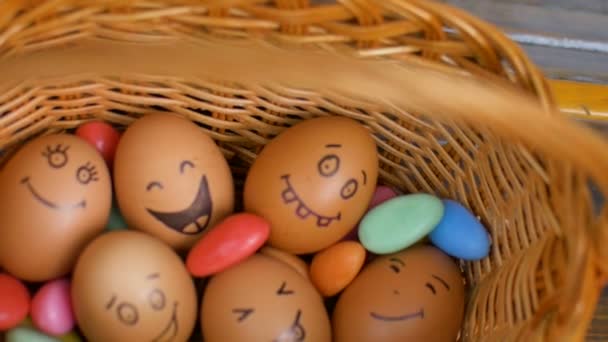 Pila de huevos sonrientes dibujados a mano en la cesta de paja con dulces de colores, preparación de Pascua, conceptos de humor de vacaciones - Imágenes, Vídeo