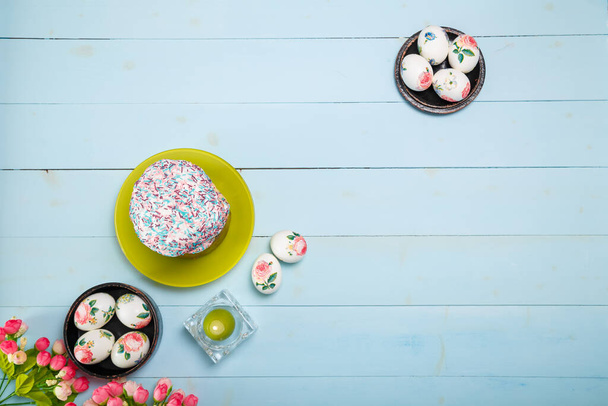 Easter decorated eggs, flowers, burning candle and Easter bread or cake with glaze and multicolored sugar sprinkles. Top view, flatlay, copy space. - Photo, Image