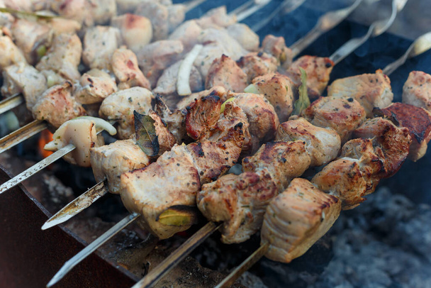 Miękkie skupione ujęcie marynowanych kawałków mięsa wieprzowego na szaszłykach smażących się nad ogniskiem. Kebab lub tradycyjne shashlik gotowanie z dużą ilością dymu. - Zdjęcie, obraz