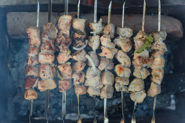 Soft focused shot of marinaded pork meat pieces on skewers frying over bonfire. Kebab or traditional shashlik cooking with lot of smoke. Top view - Photo, Image