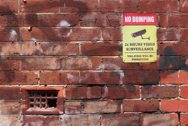 vermelho, amarelo e preto Sem Dumping, 24 horas de vigilância por vídeo, os violadores serão perseguidos sinal de aviso em uma parede de tijolo - Foto, Imagem