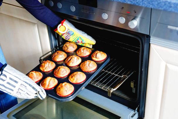 Vista aérea de una bandeja para hornear con muffins de vainilla de chocolate recién preparados sostenidos por un niño - Foto, Imagen