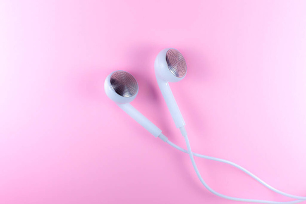 Bílá sluchátka ležící na růžovém pozadí. Moderní hudební koncept. Audio technologie. Zavřít fotografii. - Fotografie, Obrázek