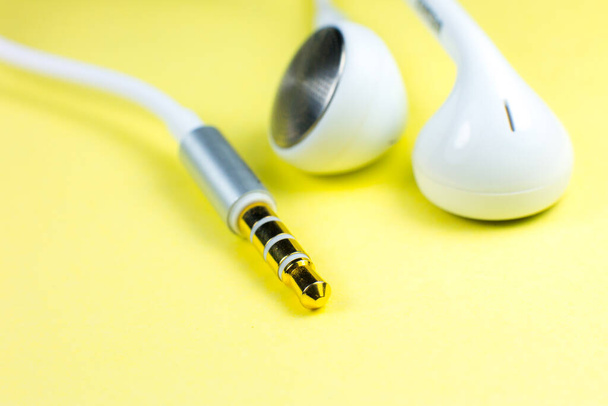 Valkoiset kuulokkeet makaavat keltaisella taustalla. Modernin musiikin konsepti. Äänitekniikka. Sulje kuva. - Valokuva, kuva
