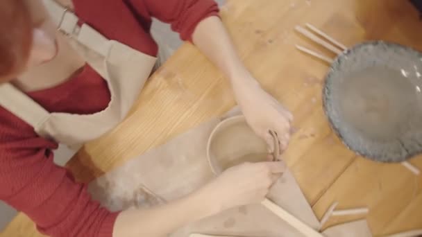 Top panning záběr rukou samice hrnčíř vyhlazování vnitřní povrch ručně vyrobené hliněné mísy s jemnými pohyby hladící palec, a dřevěné nástroje ležící na stole - Záběry, video