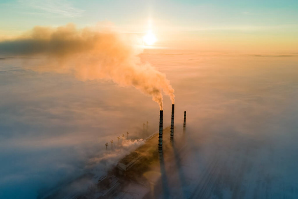 Воздушный обзор высоких труб угольной электростанции с черным дымом, движущимся вверх загрязняющей атмосферу на закате. - Фото, изображение