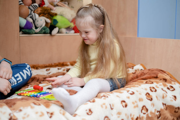 Desarrollo armonioso de un niño con síndrome de Down. Musicoterapia para niños con síndrome de Down. Una chica con síndrome de Down toca el scylophone en su casa. - Foto, Imagen